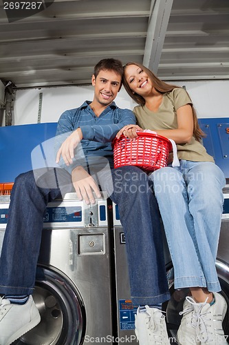 Image of Couple With Laundry Basket Sitting On Washing Machines