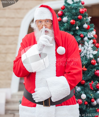 Image of Santa Claus With Finger On Lips Against Christmas Tree