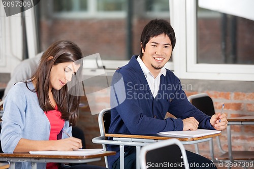 Image of Student Sitting At Desk With Classmate In Classroom