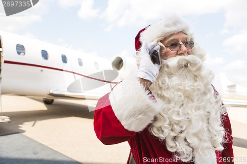 Image of Santa Claus Communicating On Mobile Phone Against Private Jet