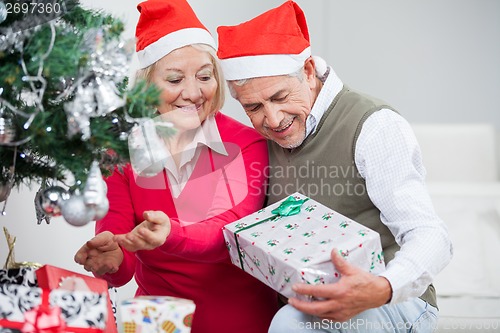 Image of Senior Couple Looking At Present While Decorating Christmas Tree
