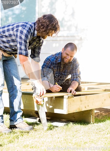 Image of Workers Measuring Wood At Construction Site