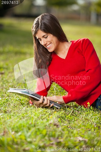 Image of Student Reading Book While Relaxing On Grass At Campus