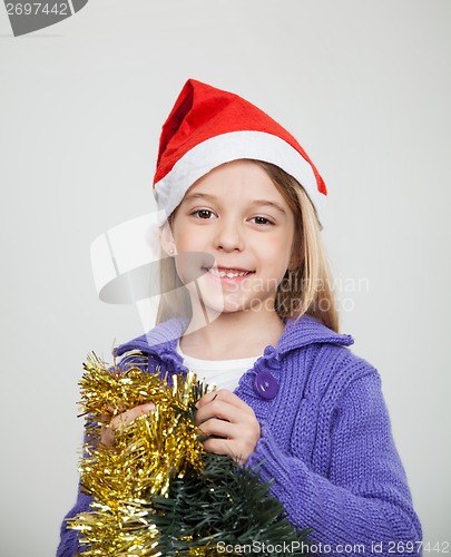 Image of Smiling Girl Wearing Santa Hat Holding Tinsels