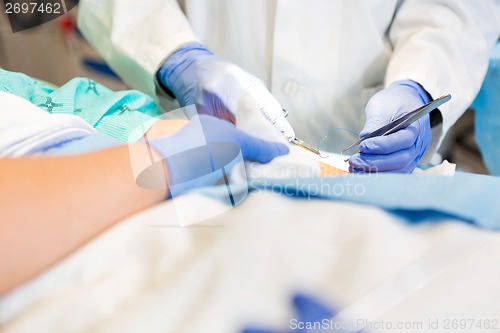 Image of Doctor Stitching Patient's Wound While Nurse Assisting Him