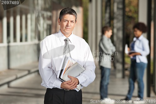 Image of Confident Professor With Books Standing On College Campus