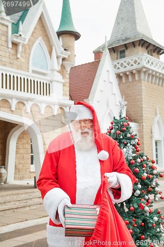 Image of Santa Claus Putting Gift In Bag Outside House