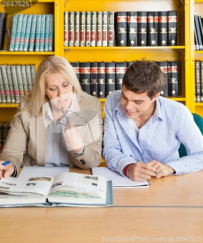 Image of Teacher And Student Looking At Book While Sitting In Library