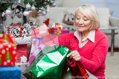 Image of Woman Looking In Bag While Sitting By Christmas Presents