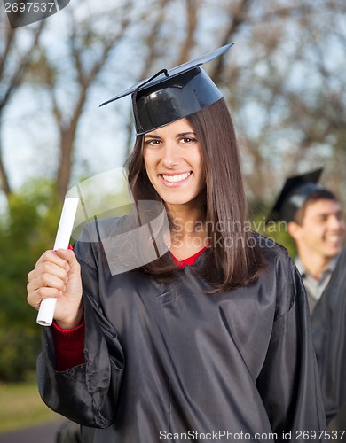 Image of Woman In Graduation Gown Holding Diploma On College Campus