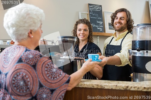 Image of Waitress With Colleague Serving Coffee To Woman At Counter