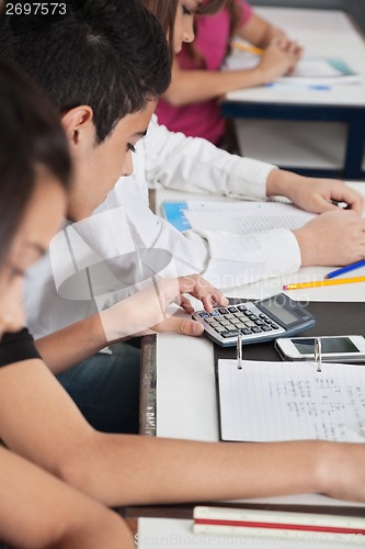 Image of Schoolboy Using Calculator At Desk