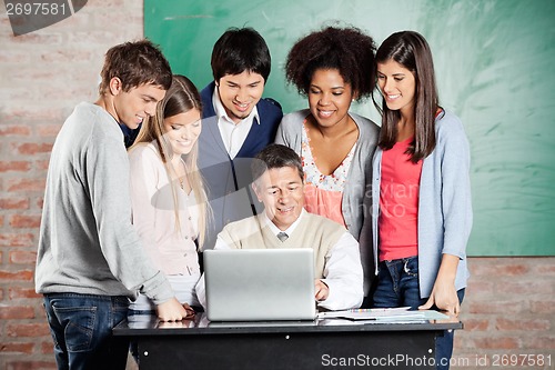 Image of Professor And Students Looking At Laptop In Classroom