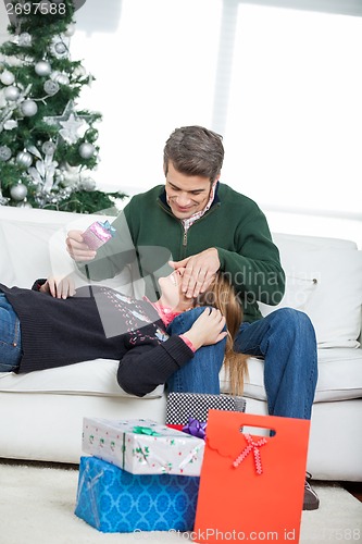 Image of Man Covering Woman's Eyes While Holding Christmas Gift