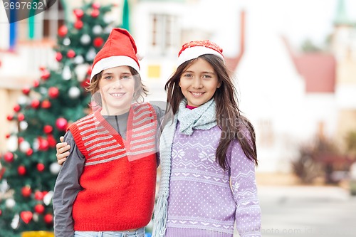 Image of Friends In Santa Hat Standing Against Christmas Tree