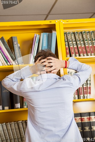 Image of Frustrated Man Standing Against Bookshelf In Library