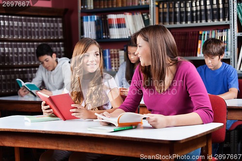 Image of Female Friends Looking At Each Other While Sitting In Library