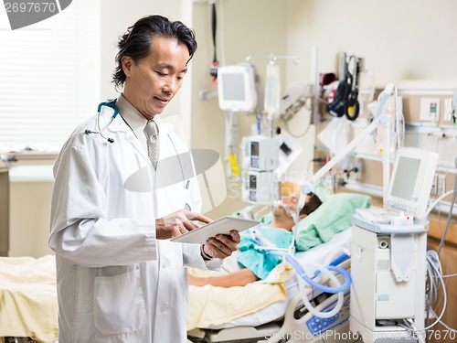 Image of Doctor Using Digital Tablet While Patient Resting In Hospital