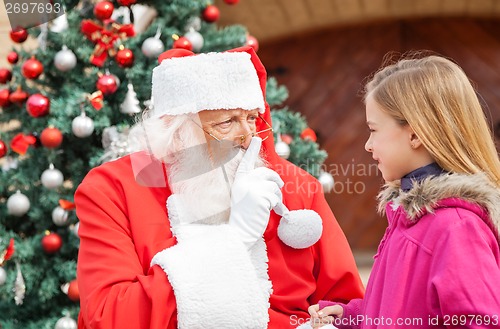 Image of Santa Claus Gesturing Finger On Lips While Looking At Girl