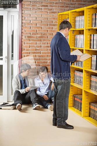 Image of Librarian Reading Book While Students Using Digital Tablet In Li