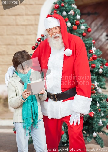 Image of Santa Claus Standing With Boy Using Digital Tablet