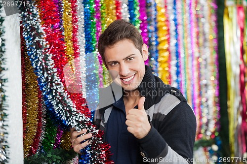 Image of Man Gesturing Thumbs Up While Holding Tinsels At Store