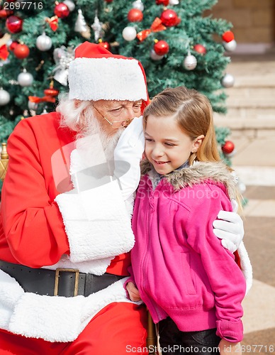 Image of Santa Claus Whispering In Girl's Ear Against Christmas Tree