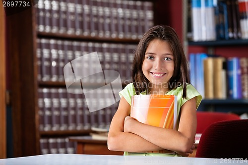 Image of Cute Schoolgirl Holding Book While Sitting In Library