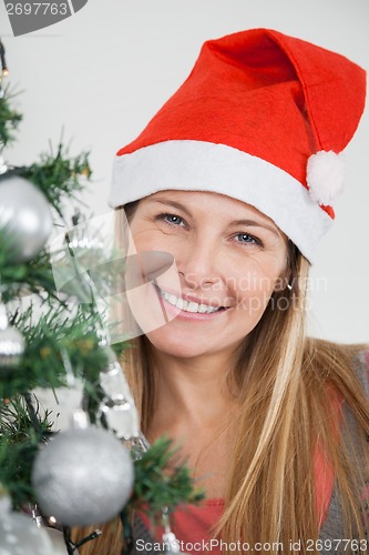 Image of Woman In Santa Hat Smiling By Christmas Tree