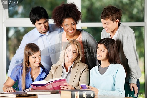 Image of Professor And Students Discussing Over Book In Classroom