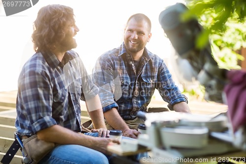 Image of Workers Holding Disposable Coffee Cups While Sitting On Frame