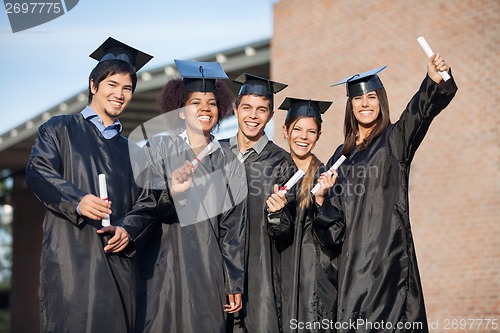 Image of Students In Graduation Gowns Holding Diplomas On University Camp