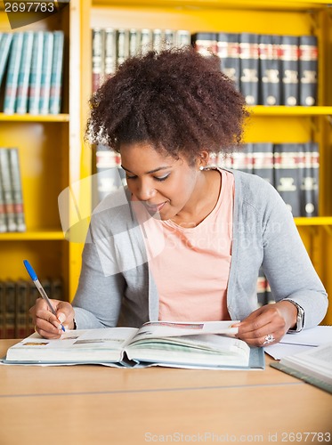 Image of Student Writing In Book At Library