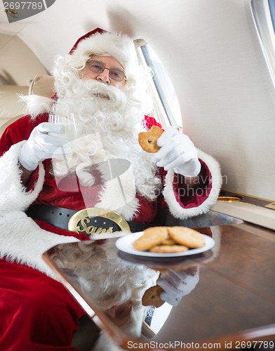 Image of Santa Eating Cookies While Holding Milk Glass In Private Jet