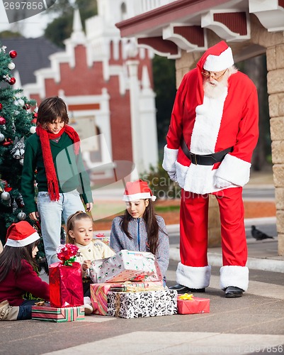 Image of Santa Claus Looking At Children Opening Gifts