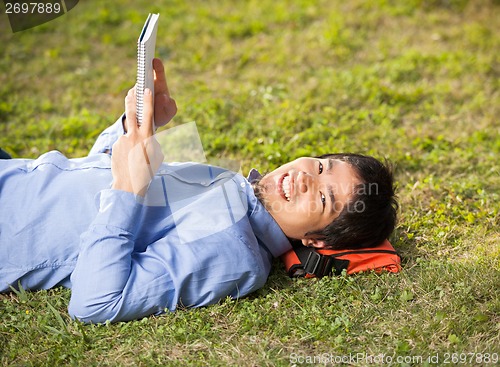 Image of Student Holding Book While Lying On Grass At Campus