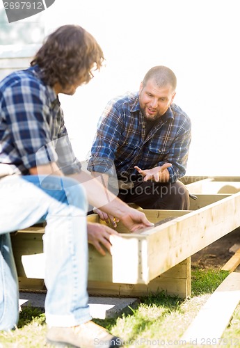 Image of Carpenter Communicating With Coworker Measuring Wooden Frame