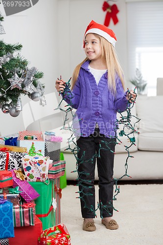 Image of Girl Holding Fairy Lights While Standing By Christmas Gifts