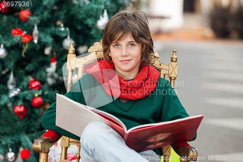 Image of Boy With Book Sitting Against Christmas Tree