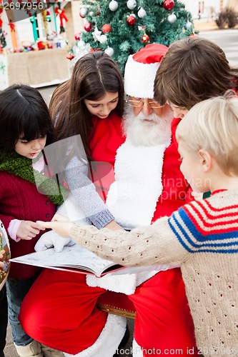 Image of Santa Claus With Children Pointing At Book