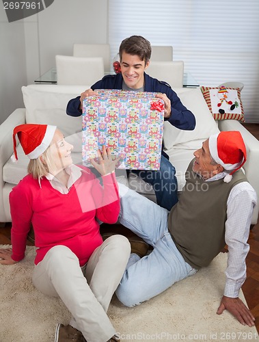 Image of Man Holding Christmas Present While Parents Looking At Him