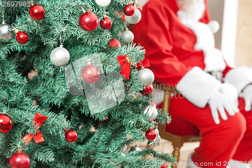 Image of Decorated Christmas Tree With Santa Claus Sitting In Background