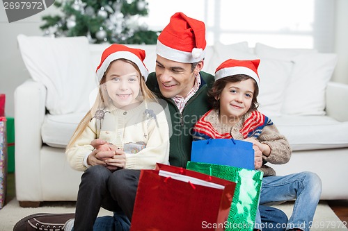 Image of Siblings Sitting On Father's Lap With Christmas Presents