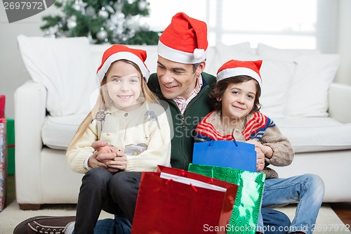 Image of Siblings Sitting On Father's Lap With Christmas Presents