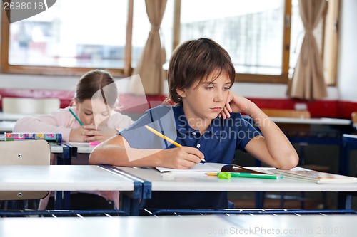 Image of Boy Looking Away While Writing In Book