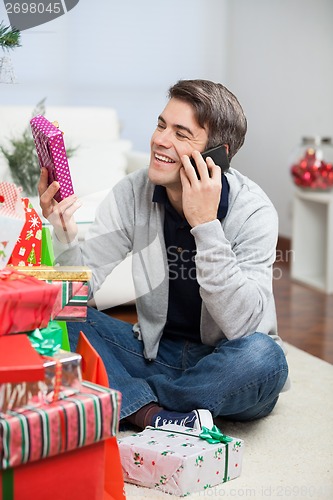 Image of Man Holding Christmas Gift While Answering Mobilephone