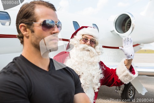 Image of Santa Waving Hand With Bodyguard In Foreground Against Private J