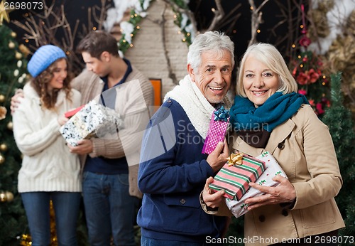 Image of Senior Couple Holding Christmas Presents With Children In Store