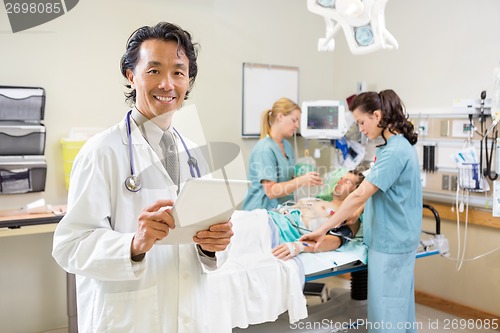 Image of Doctor Holding Digital Tablet With Nurses Examining Patient