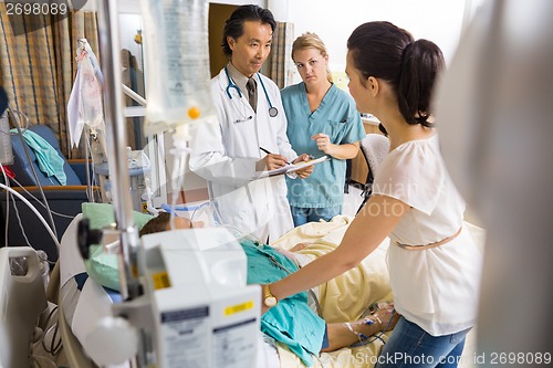 Image of Woman Standing By Patient's Bed Looking At Doctor And Nurse
